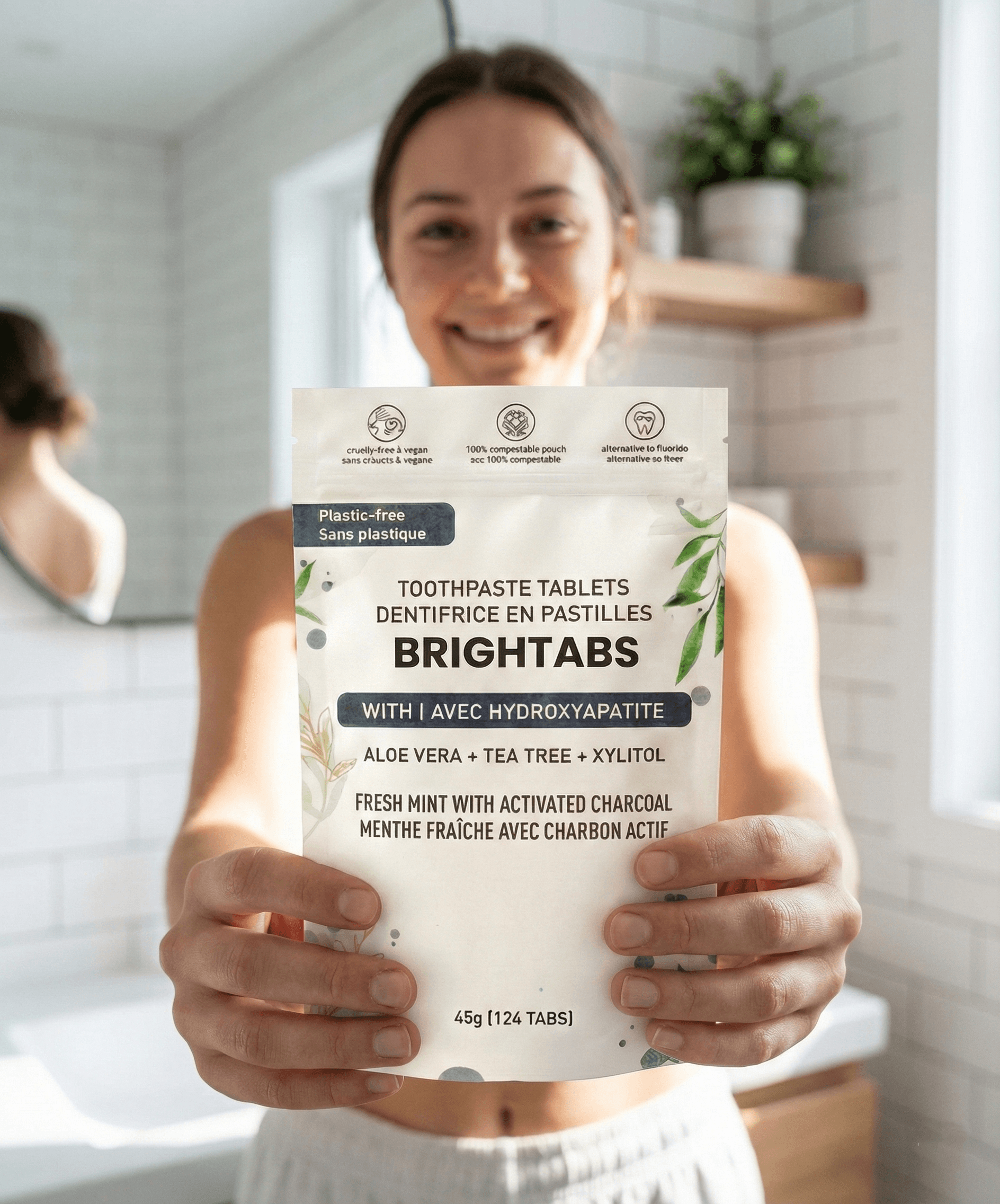 A woman holding the BRIGHTABS Toothpaste Tablets pouch in a bathroom.
